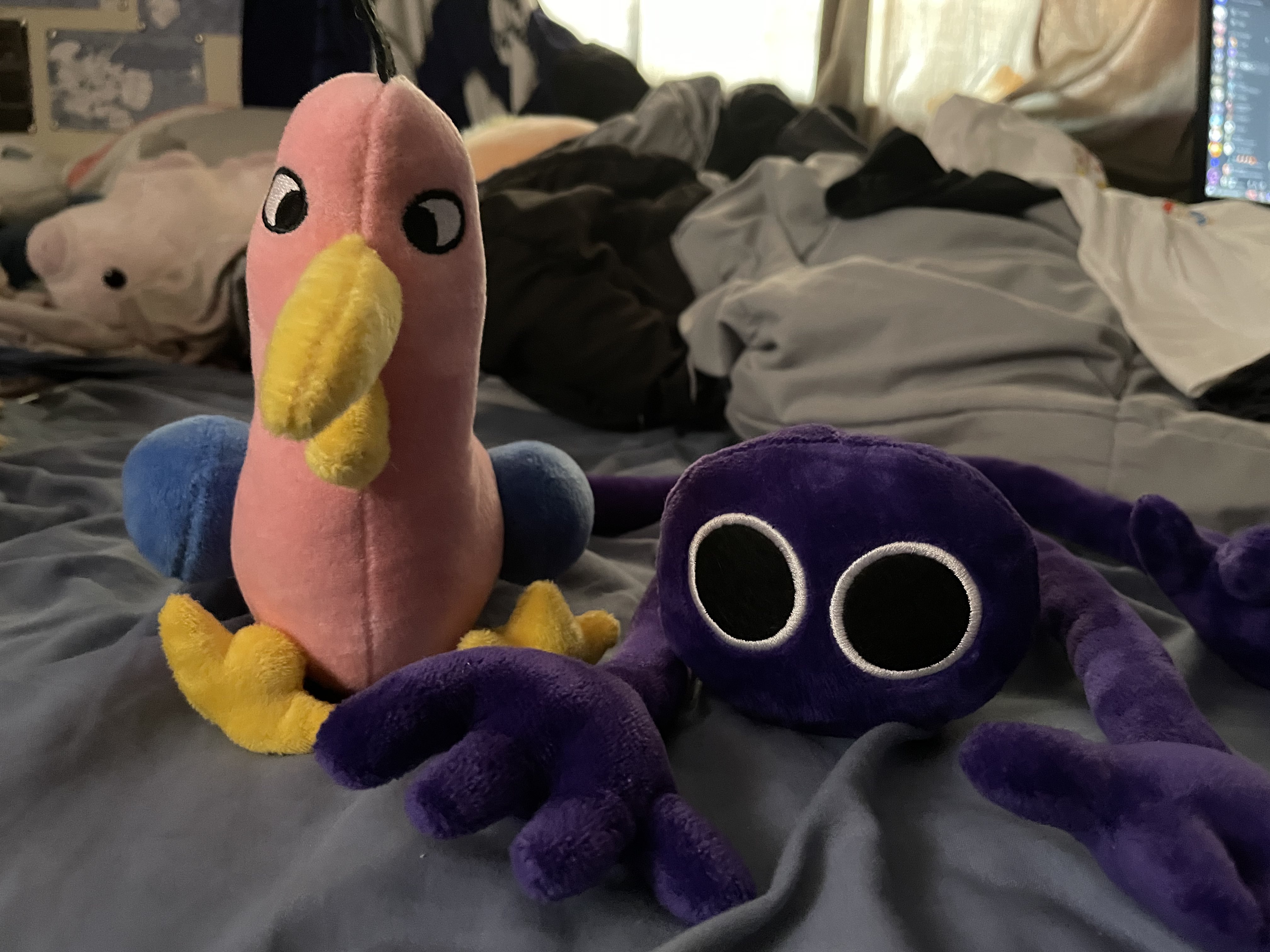 AN IMAGE OF BOTH OF THE PLUSHIES (OPILA BIRD FROM GARTEN OF BANBAN AND PURPLE FROM RAINBOW FRIENDS) I BOUGHT SITTING NEXT TO EACH OTHER.