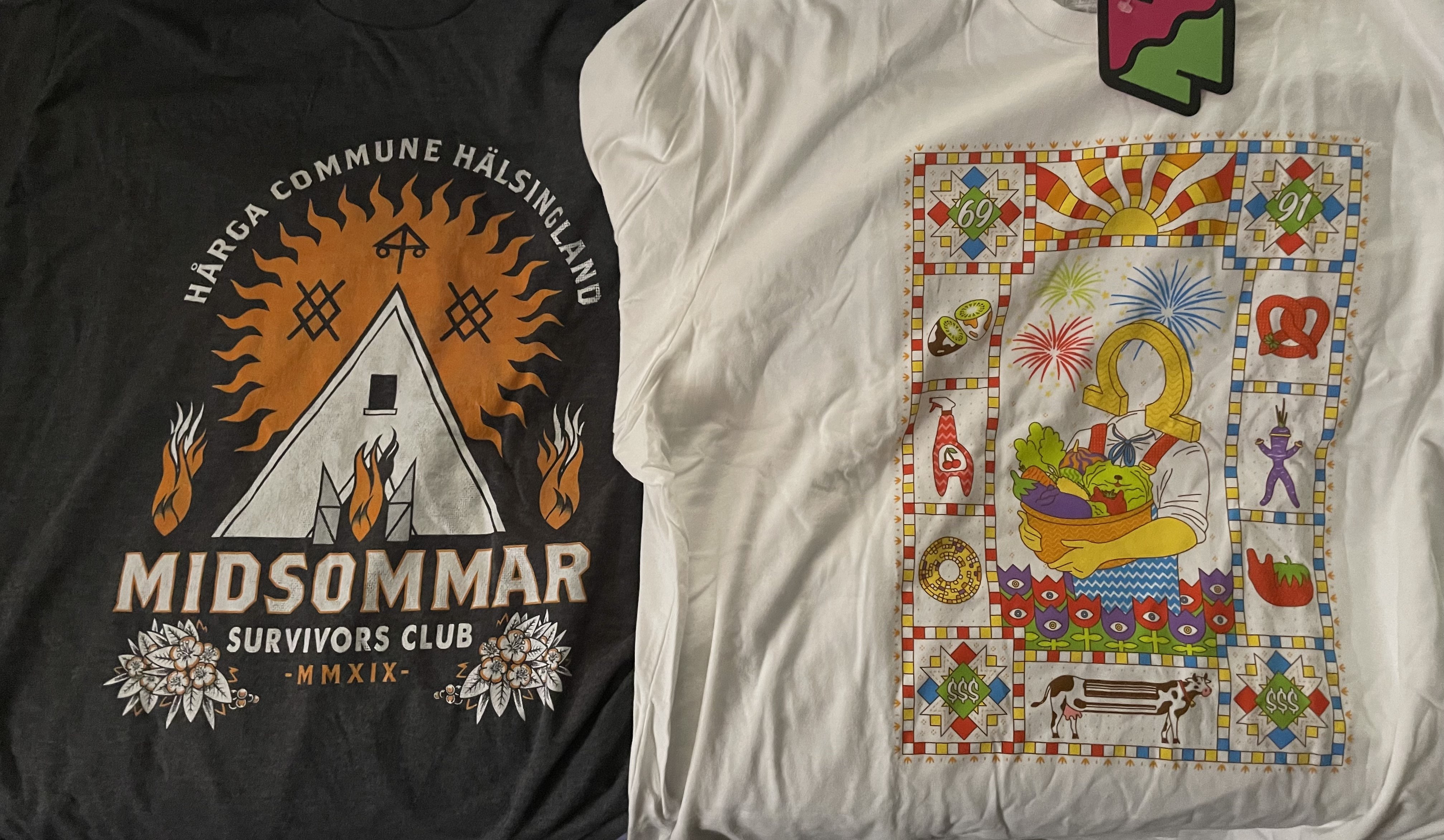 AN IMAGE OF TWO OF THE SHIRTS I RECIEVED FOR MY BIRTHDAY. ON THE LEFT IS A MIDSOMMAR PRINT WITH THE TENT IN THE MIDDLE. THE TOP CAPTION READS 'Hårga COMMUNE HÄLSINGLAND' WHILE THE BOTTOM CAPTION READS 'MIDSOMMAR, SURVIVORS CLUB, MMXIX'. FLAMES, FLOWERS AND RELEVANT RUNES ARE ALSO ON THE PRINT. THE SHIRT ON THE RIGHT IS OF MEOW WOLF OMEGAMART'S MASCOT MR. OMEGA, HOLDING A BASKET OF VEGETABLES. SEVERAL OTHER OMEGAMART-RELEVANT GRAPHICS SURROUND HIM IN A QUILT PATTERN, INCLUDING THE LONG COW, A DAIKON, THE CHERRY BLITZ SPRAY AND MORE.